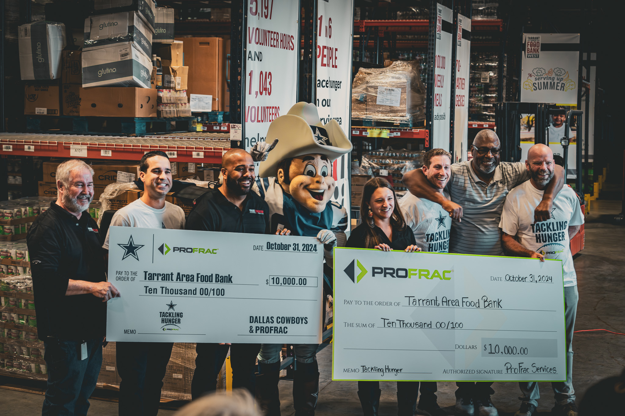 The executive team, Rowdy the Cowboy, Dallas Cowboy executives, Charles Haley and others are presenting donation checks to The Tarrant Area Food Bank