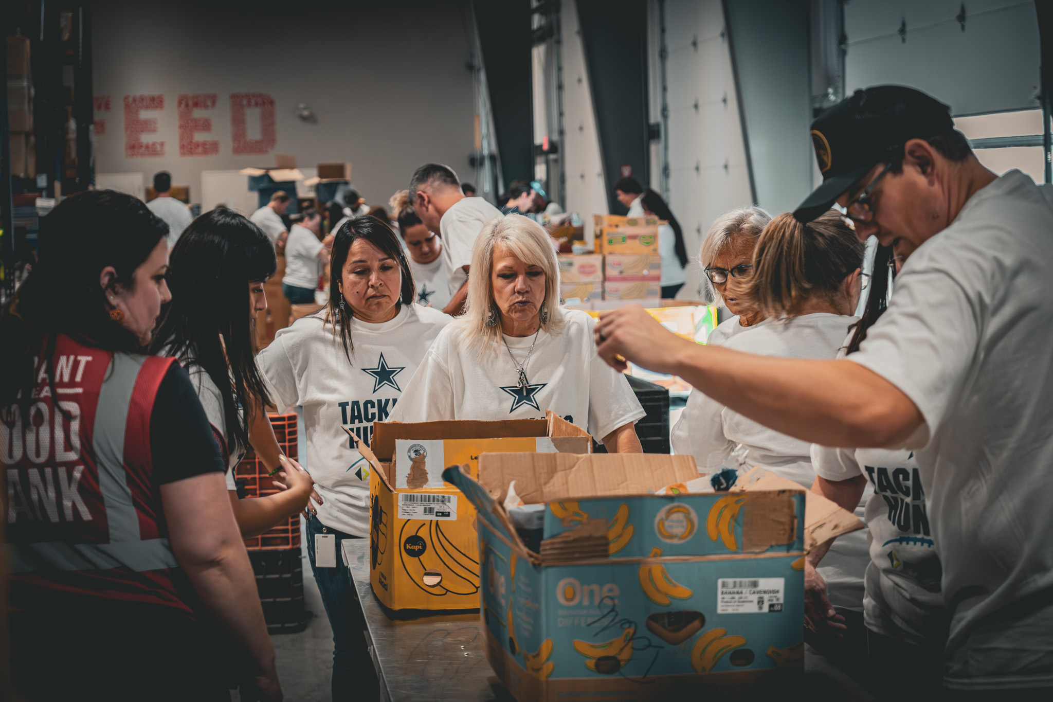 Volunteers from ProFrac services and the Dallas Cowboys and community members pack food boxes at the Tarrant Area Food Bank during a charitable event to fight hunger
